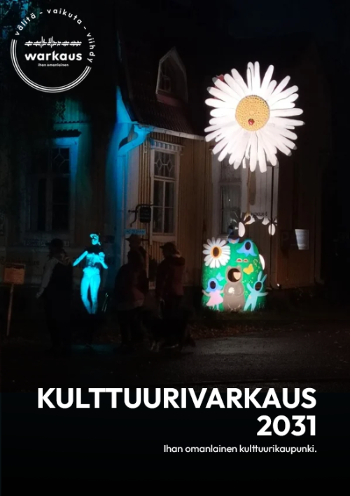 Tummalla taustalla valaistu rakennus ja patsas. Teksti: KulttuuriVarkaus 2031 - ihan omanlainen kulttuurikaupunki.