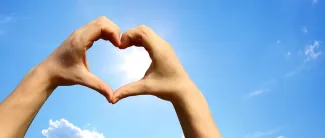 Sormet käännettyinä sydämen muotoon, taustalla sininen taivas.