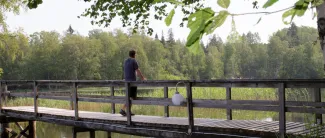 Mies nojaa puisen sillan kaiteeseen ja katselee järvelle.