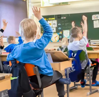 Peruskoululaisia viittaamassa luokassa.