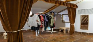 Kuvassa esiripun takaa näkyvä vaaterekki, jossa erilaisia sovitettavia vaatteita.