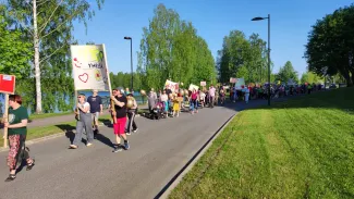 Kulkueessa kymmeniä ihmisiä. Etualalla nurmikkoa, taustalla puita.