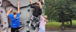 Kolme tyttöä kiipeilee liikennepuiston seinäkiipeilyseinällä.