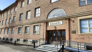 punatiilinen kolmikerroksinen rakennus jossa on paljon pieniruutuisia ikkunoita puolikaaren muotoisen ikkunan alla on kylrri jossa lukee konsti.