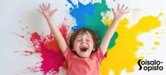 Iloinen pieni lapsi on kädet ylhäällä ja taustalla suuria väriläiskiä