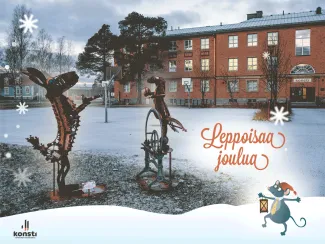 kuvassa on punatiilinen iso rakennus ja etualalla metallista tehty veistos jossa jänis ja saukko sekä teksti leppoisaa joulua!